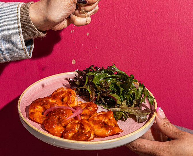 Plate of grilled greens with salsa on a pink background