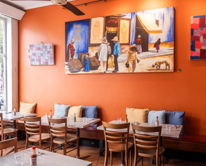 Orange wall with framed artwork above bench seating at Baja Cantina