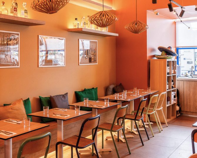 Dining nook with orange walls and green cushions at Baja Cantina