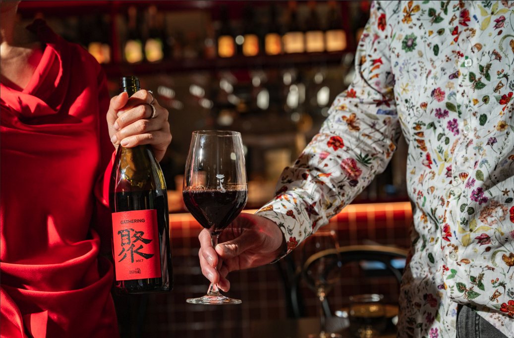 A glass of red wine poured beside a bottle of Gathering red at the Lucky You Darling bar